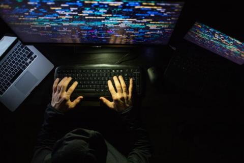 a hacker sits in the dark surrounded by monitors to symbolize preventing intellectual property theft with AI and natural language processing